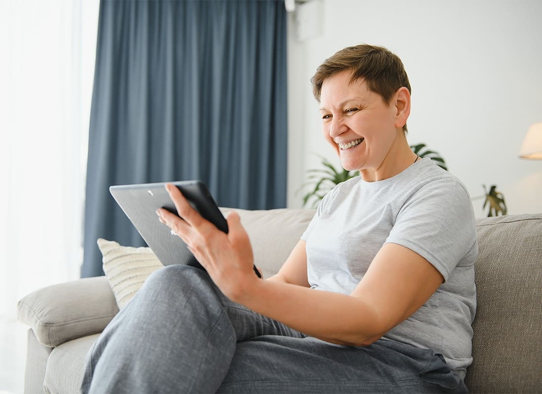 Blog - Cheerful Middle Aged Woman Sitting on the Sofa While Reading on a Tablet